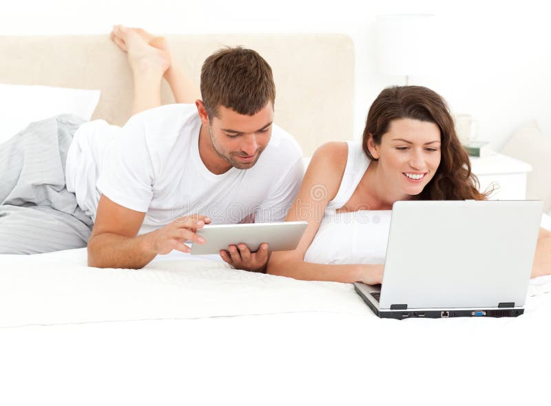 Cute couple working together on their laptop lying on their bed at home