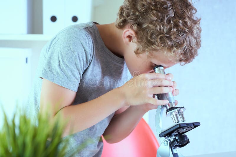 Cute elementär skolpojke som tittade på mikroskop vid sitt skrivbord i laboratoriet Unga forskare som gör experiment på royaltyfri bild
