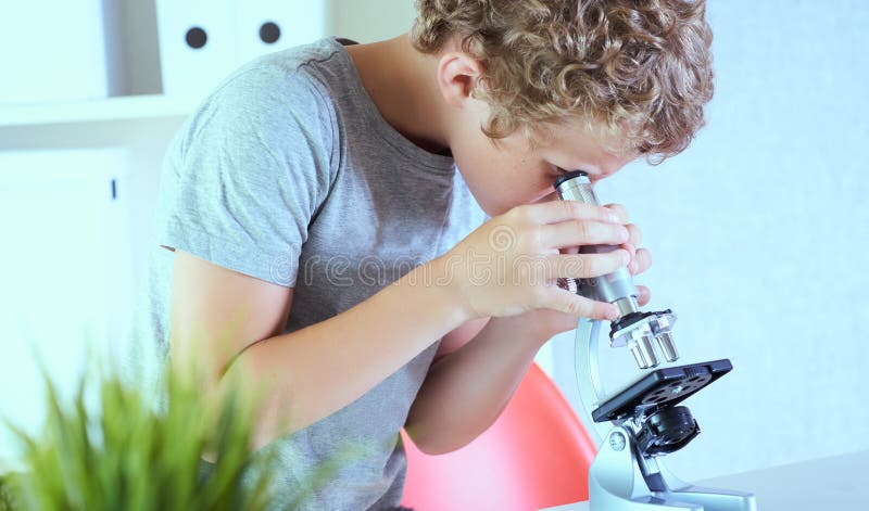 Cute elementär skolpojke som tittade på mikroskop vid sitt skrivbord i laboratoriet Unga forskare som gör experiment på arkivbild
