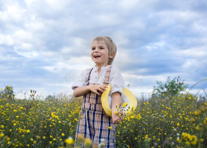 Cute enthusiastic cheerful boy dressed in a rustic style stands in a field of wild yellow flowers. Summer mood