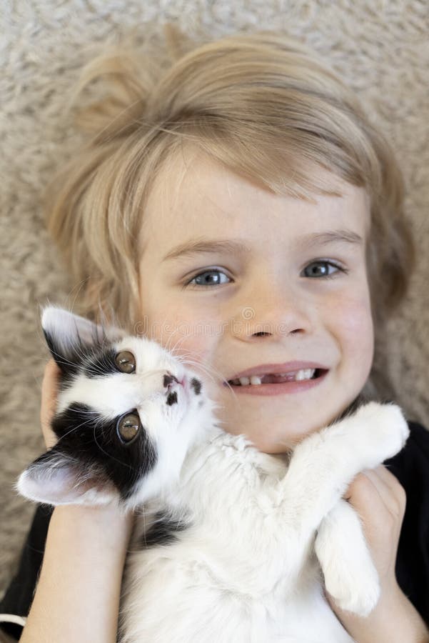 cute face of a contented blond boy and a black and white kitten