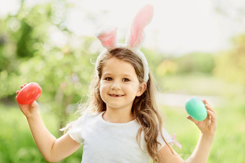 Cute funny girl with Easter eggs and bunny ears at garden. easter concept. Laughing child at Easter egg hunt