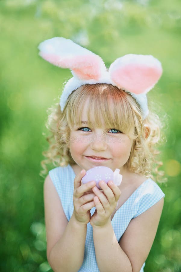 Cute funny girl with Easter eggs and bunny ears at garden. easter concept. Laughing child at Easter egg hunt