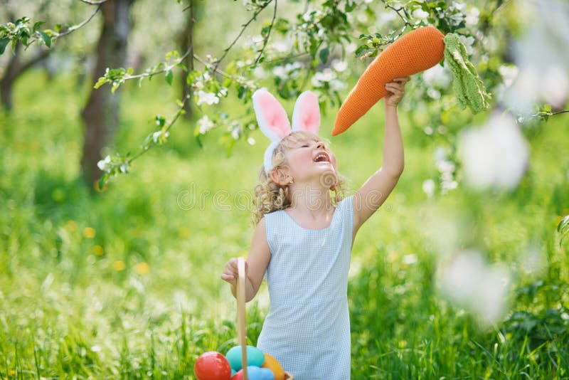 Cute funny girl with Easter eggs and bunny ears at garden. easter concept. Laughing child at Easter egg hunt