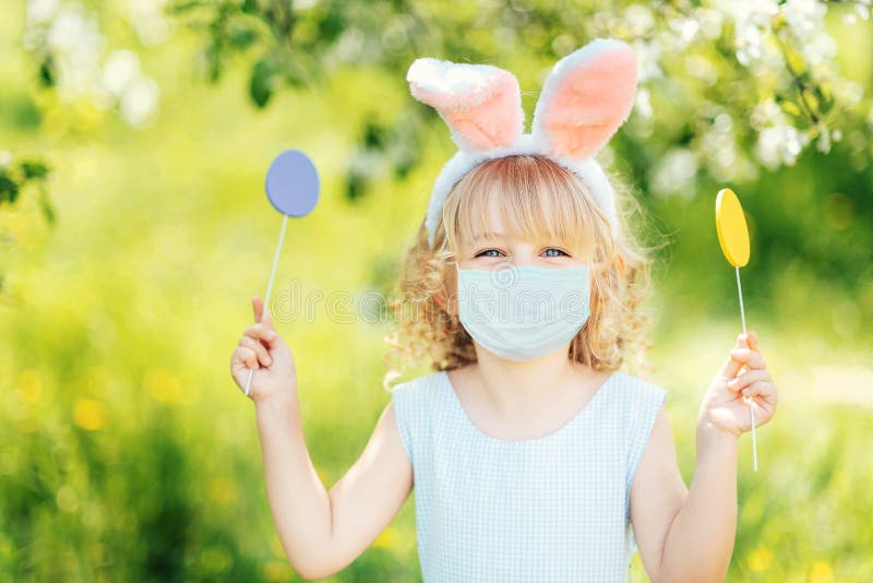 Cute funny girl with Easter eggs and bunny ears wearing medicine mask at garden