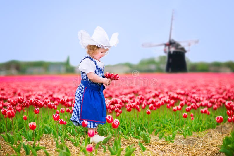 Cute girl in Dutch costume in tulips field with windmill