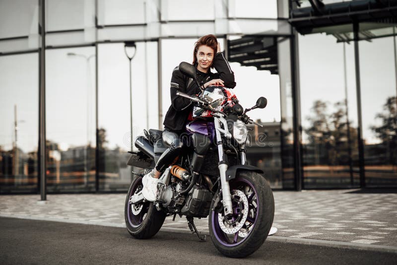 Cute girl in a motorcycle jacket sits with a motorcycle helmet on a motorbike