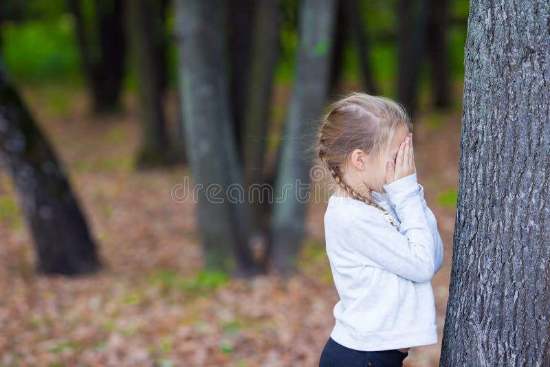 Little girl playing hide and seek in autumn forest outdoors. Little girl playing hide and seek in autumn forest outdoors