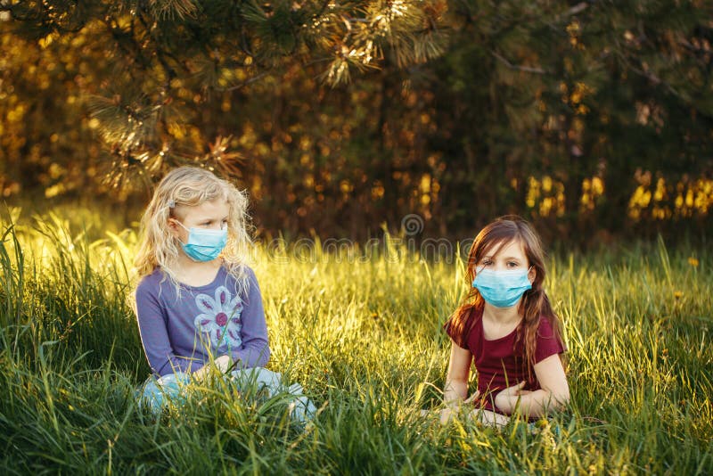 Cute girls friends in sanitary masks on faces. Preschool children kids wearing protective mask against coronavirus. Social  physical distance and health protection during covid-19 quarantine. Cute girls friends in sanitary masks on faces. Preschool children kids wearing protective mask against coronavirus. Social  physical distance and health protection during covid-19 quarantine