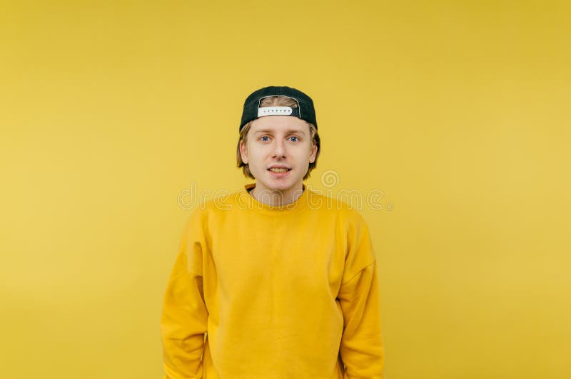 Cute guy in a cap and casual clothes isolated on a yellow background, looking at the camera and smiling royalty free stock image