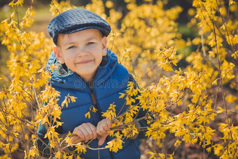 Cute handsome boy in stylish blue dress and hat close to yellow flowers enjoying spring time.