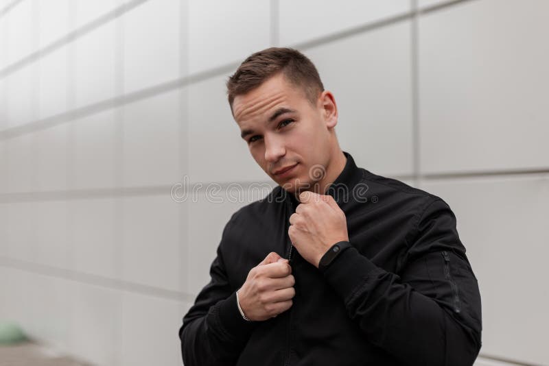Cute handsome young man in a fashionable black jacket posing standing near a modern building outdoors. European attractive guy stock image Cute handsome young man in a fashionable black jacket posing standing near a modern building outdoors. European attractive guy stock image