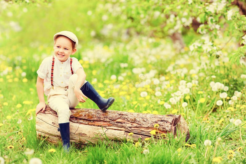 Cute happy boy sitting on wooden stump in spring garden