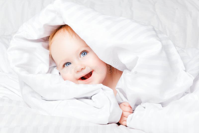 Cute and Happy child with blue eyes looking out of the white blanket. Copy space. royalty free stock image Cute and Happy child with blue eyes looking out of the white blanket. Copy space. royalty free stock image