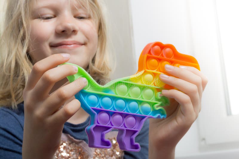 Cute happy girl holds rainbow pop it in the form of a dinosaur stock photos