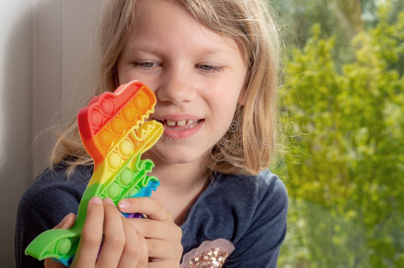 Cute happy girl holds rainbow pop it in the form of a dinosaur stock photos