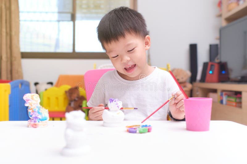 Cute happy little Asian toddler boy child  painting color on DIY plaster painting toy, 3D plaster statue indoor at home, Creative