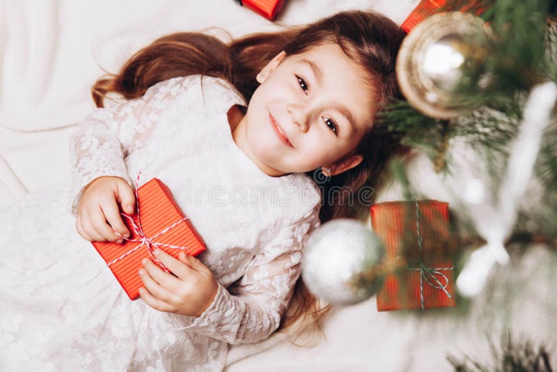 Cute happy little girl Laughing in Christmas atmosphere with gift boxes and magic lights. Happy child holding her Christmas present. Cute happy little girl Laughing in Christmas atmosphere with gift boxes and magic lights. Happy child holding her Christmas present