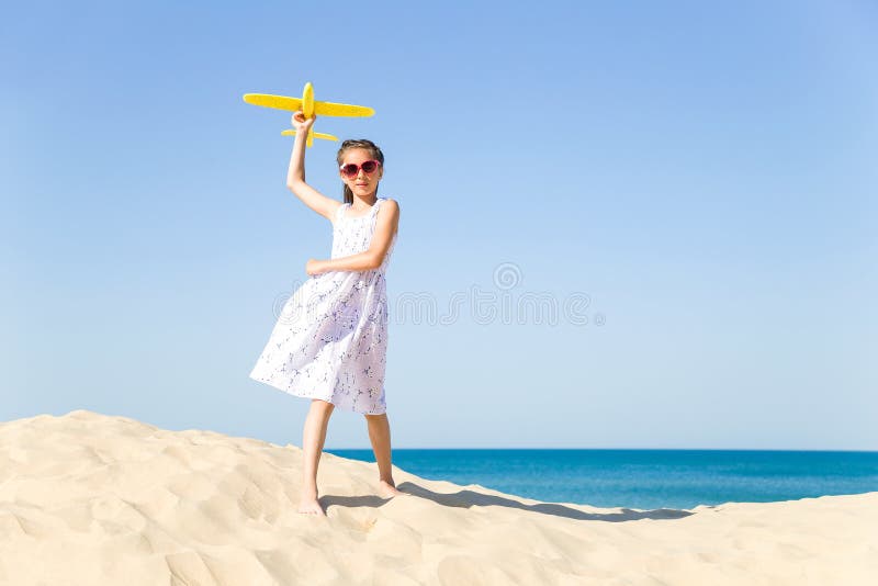 Cute happy little girl wearing sun eyeglasses and a white dress evolving in the wind playing with the yellow