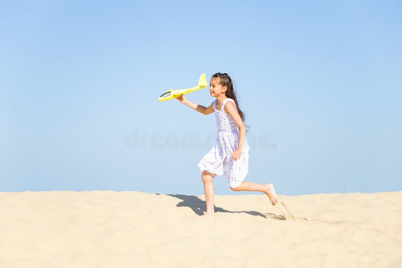 Cute happy little girl wearing a white dress running on the sandy beach by the sea and playing with the yello