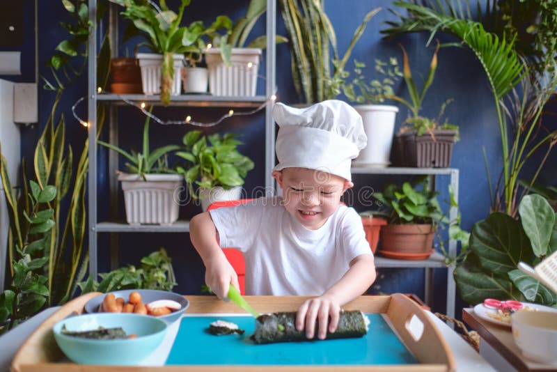 Cute happy smiling Asian little boy child wearing chef hat having fun preparing, cooking healthy Japanese food -  sushi roll at