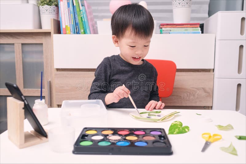 Cute happy smiling little Asian toddler boy enjoy using glue doing art project at home, Fun paper and glue crafts for toddlers