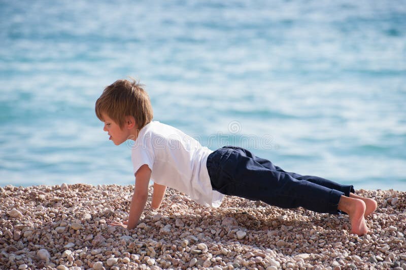 Cute healthy strong kid making pushups with effort on sea coast in autumn