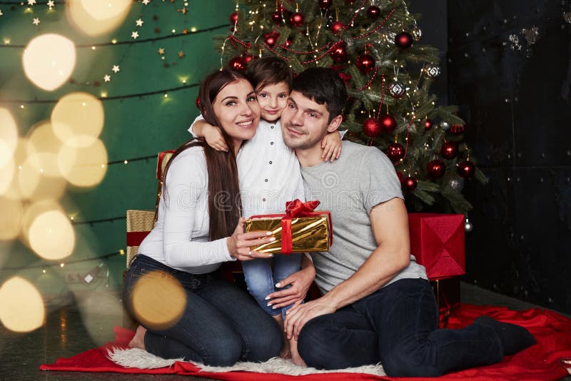 Cute hugs Familjen sitter i närheten av julgranen med presentboxar på vintern kväll, och njuter av att spendera tid royaltyfria bilder