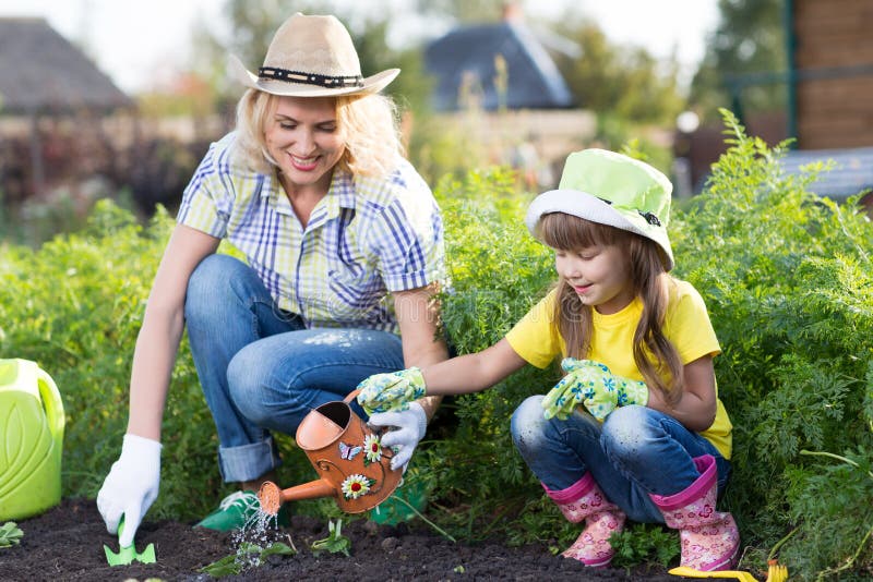 Cute kid girl helps her mother to care for plants. Mother and her daughter engaged in gardening in the backyard. Spring. Cute kid girl helps her mom to care for stock photography