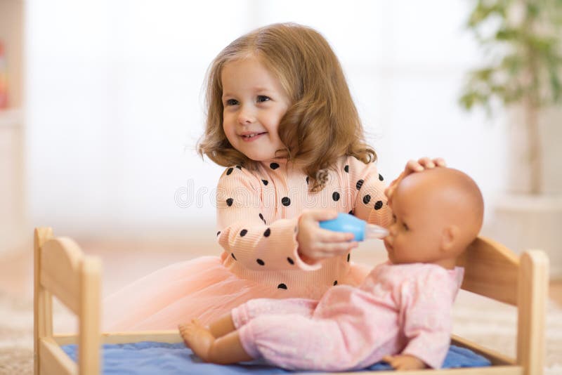 Cute kid girl playing doctor with doll at home