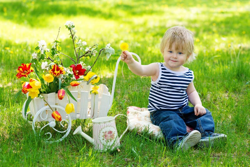 Cute kid on the grass near wheelbarrow with flowers