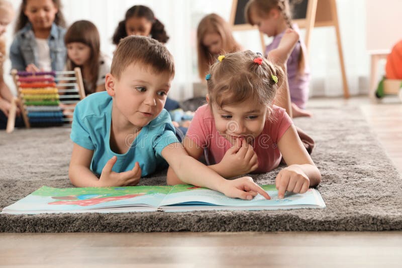 Cute kids reading book on floor while other children playing together