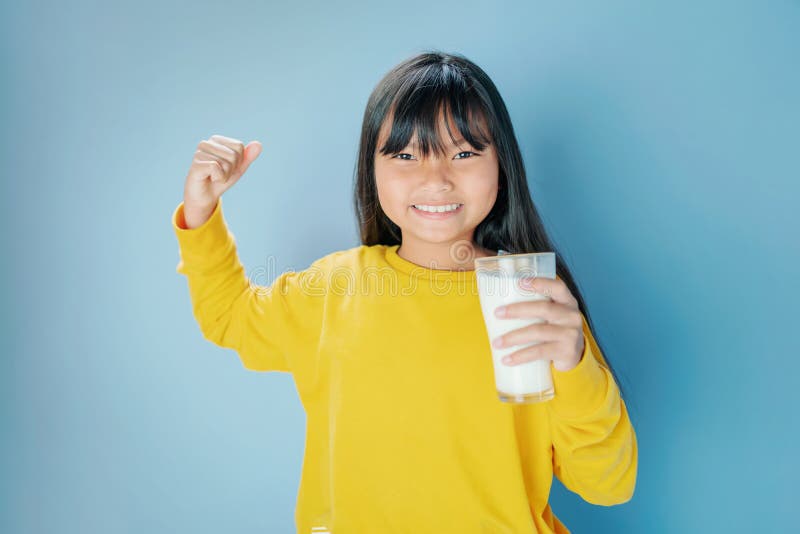 cute litle girl drinking milk in glass with smiling happy on blue