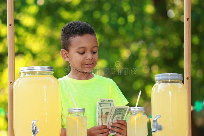 Cute little African-American boy with money at lemonade stand in park. Summer refreshing drink stock images Cute little African-American boy with money at lemonade stand in park. Summer refreshing drink stock images