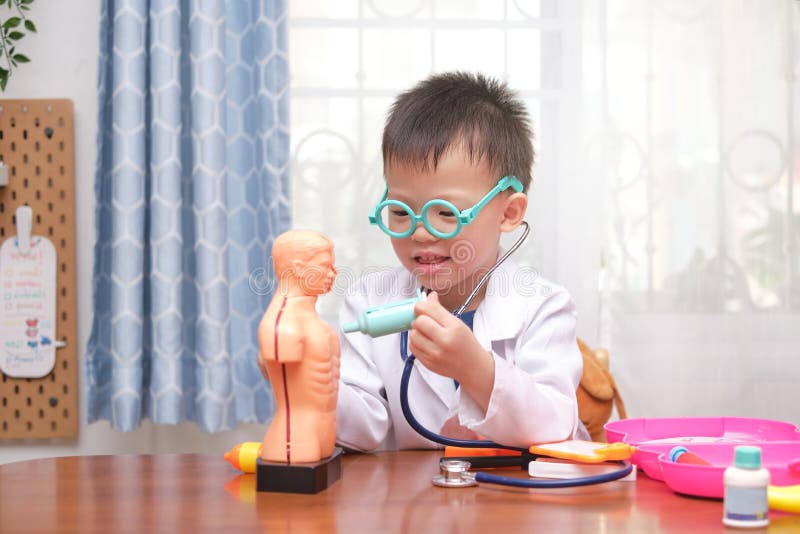 Cute little Asian school boy in doctor uniform playing doctor at home, kid wearing stethoscope learning and play with anatomical