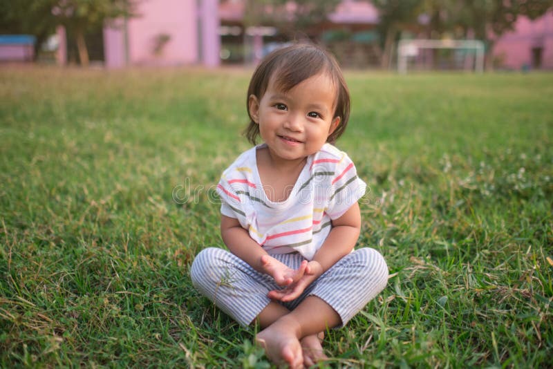 Cute little Asian 1 - 2 years old toddler baby girl child smiling at camera, barefoot practices yoga & meditating outdoors on