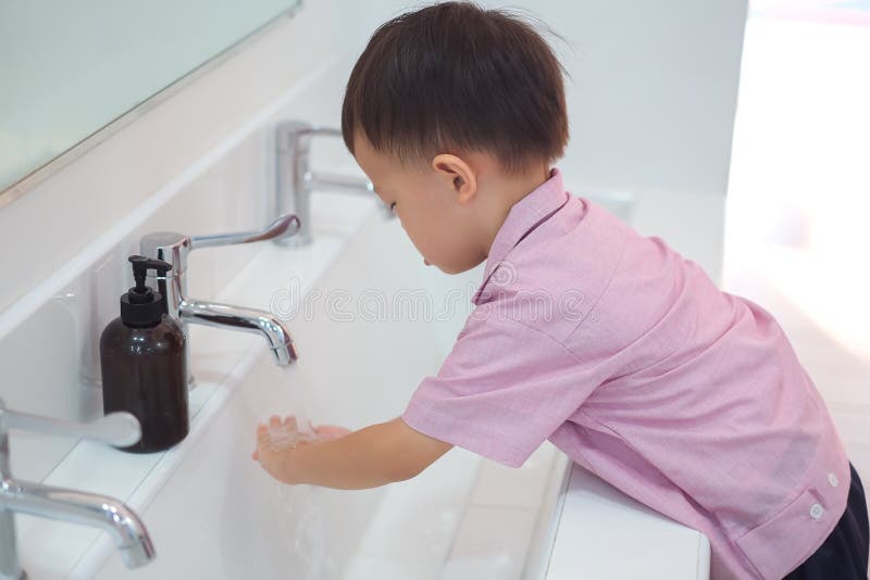 Asian 2 - 3 years old toddler boy child washing hands by himself on sink and water drop from faucet in public toilet / bathroom