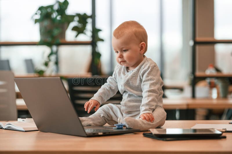 Cute Little Baby Boy is in the Modern Office on the Table by Laptop