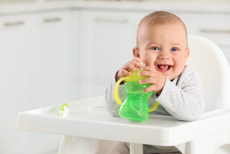 Cute little baby with sippy cup at home. Space for text