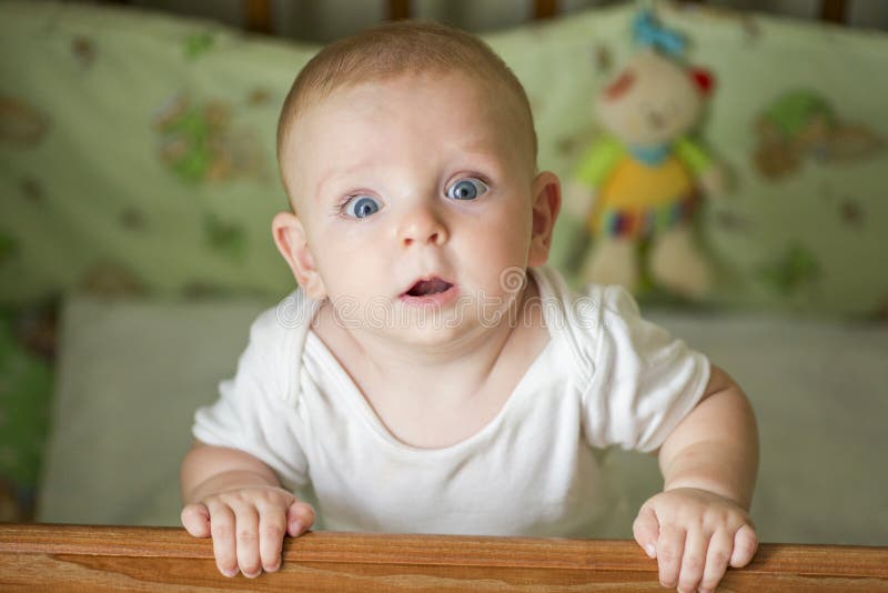 Cute little baby standing in a bed. Smiling child playing in bed. Kid portrait at nursery. Happy childhood concept