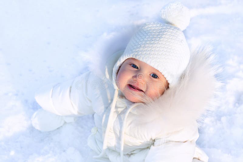 Cute little baby in a white jacket and white hat sitting in fresh winter snow royalty free stock images Cute little baby in a white jacket and white hat sitting in fresh winter snow royalty free stock images