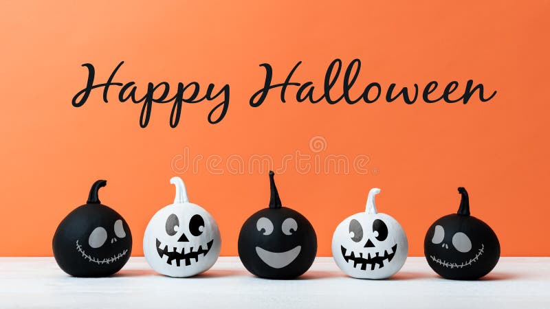 Cute Little Black and White Halloween Pumpkins with smile standing side by side on white wooden table over orange background.