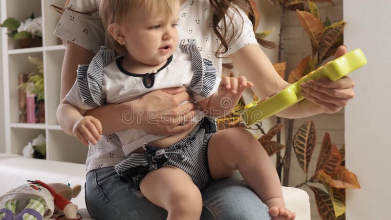 Cute little blond baby girl plays with a big interest with plastic fish sitting in her mom`s embraces slow motion