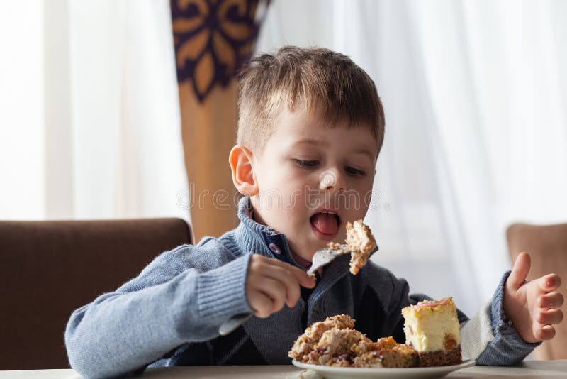 Cute little boy in cafe eat a big piece of cake with a fork. Desserts for kids