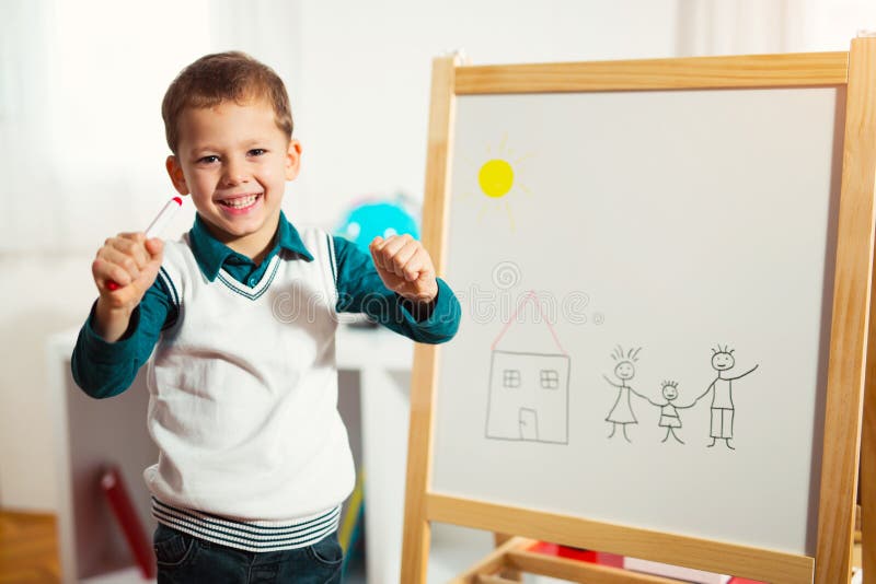 Cute little boy drawing on white board with felt pen and smiling stock photo