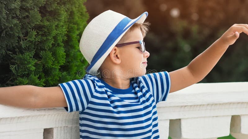 Cute little boy in hat and sunglasses showing cool gesture thumb up having good time outdoor