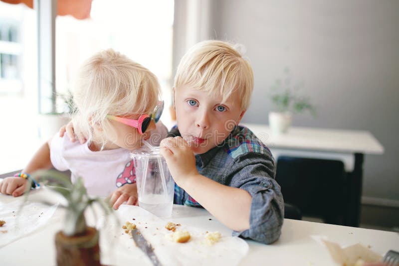 Cute little Boy and His Baby Sister are Sharing a Drink in a Coffee House Cafe