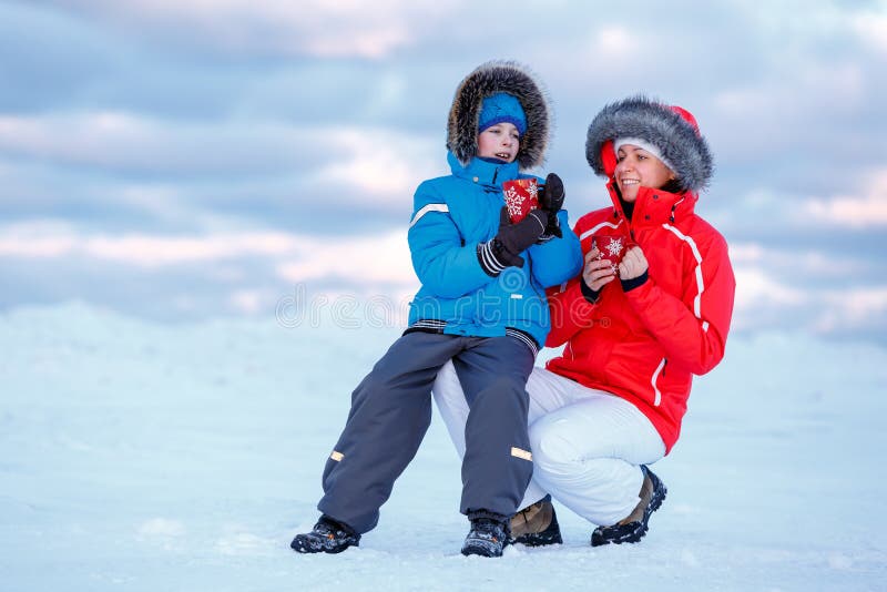 Cute little boy and his mother drinking hot tea on icy beach