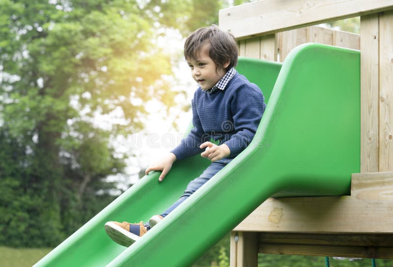 Cute little boy playing slide at the playground in retro tone, Adorable kid sitting on the slide house and looking down with surprised face, Active child playing outdoors in the sunny day on Autumn