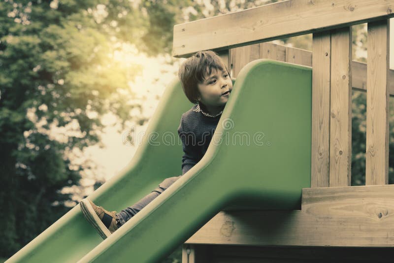 Cute little boy playing slide at the playground in retro tone, Adorable kid sitting on the slide house and looking down with surprised face, Active child playing outdoors in the sunny day on Autumn